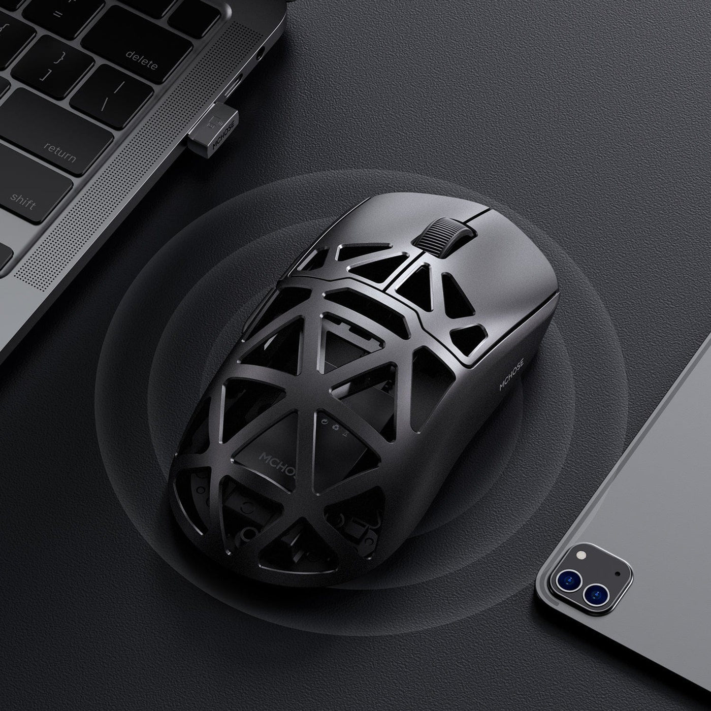 Black Mchose AX5 Pro gaming mouse on a dark surface with a laptop and smartphone in the background. Sold By Nmpc India